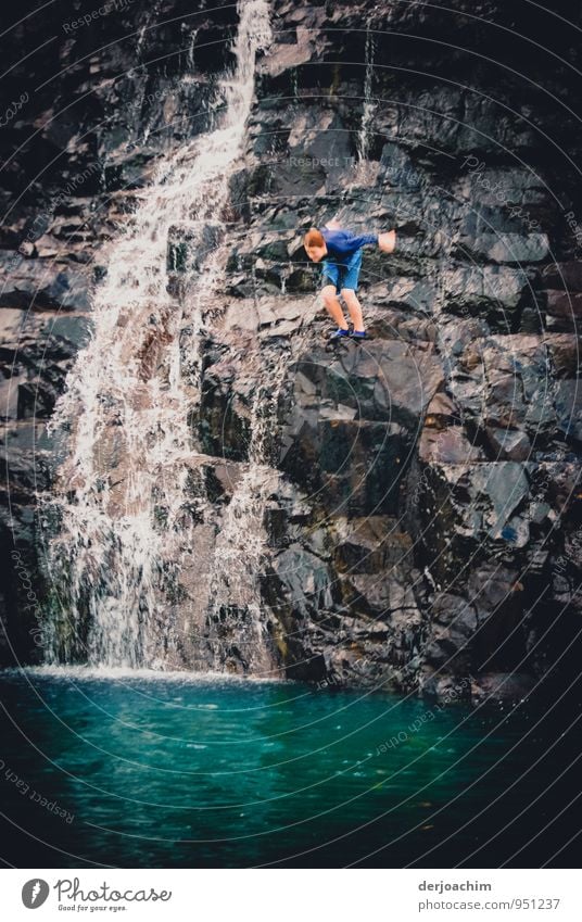 Drop down, boy jumps off a rock into a lake. There's a waterfall beside him. On the island of Prince of Wales. Torres Strait Islands.Australia Joy Contentment