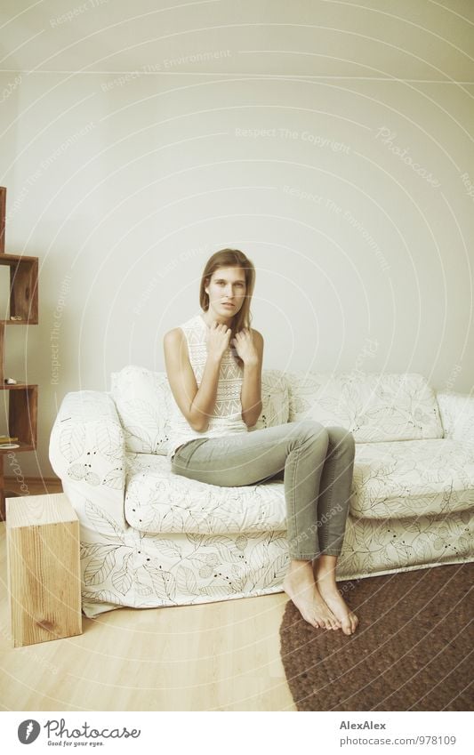 Young woman with long brunette hair and long legs sits on bed in